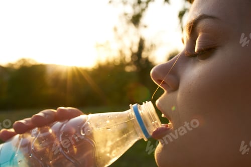 Preview: woman drinks water from a plastic bottle outdoors in summer
