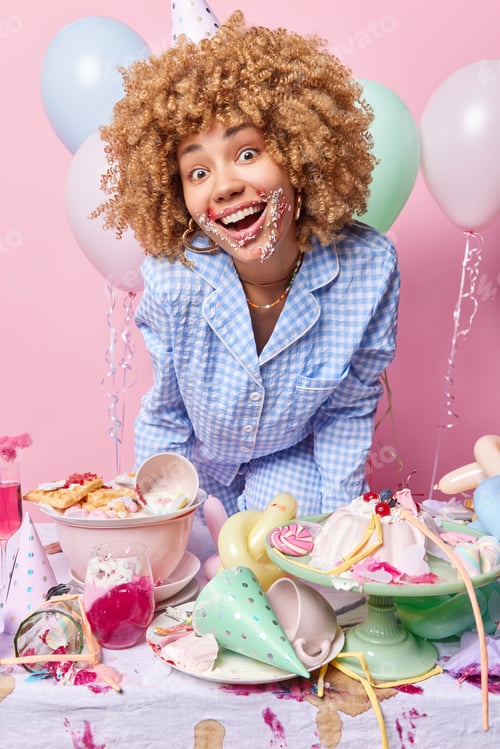 Preview: People celebration concept. Positive curly haired woman in nightwear smiles happily enjoys domestic