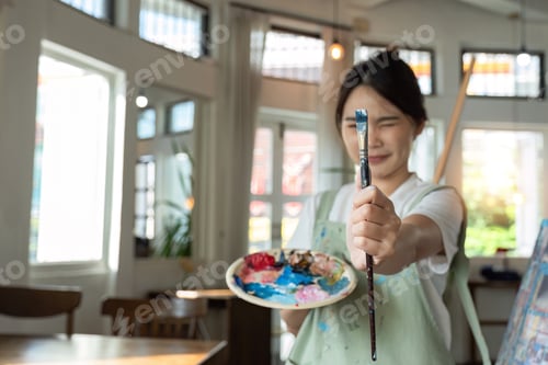 Preview: Attractive young Asian woman concentrates on painting with acrylic paints on canvas in painting