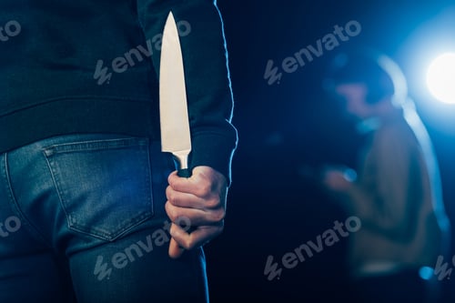 Preview: cropped view of murderer hiding knife behind back on black