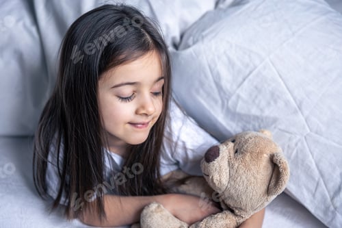 Preview: Little cute girl in bed with a teddy bear early in the morning.