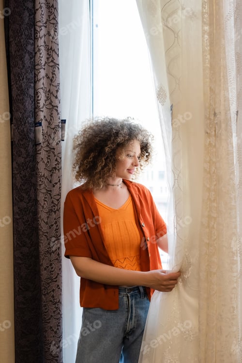 Preview: young and curly woman choosing curtains in textile shop