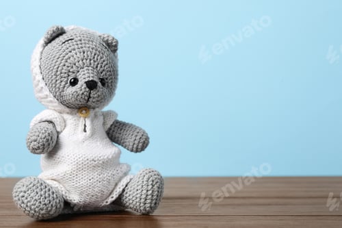 Preview: Cute knitted toy bear on wooden table against light blue background. Space for text