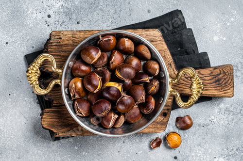 Preview: Cracked roasted chestnuts served in a skillet. Gray background. Top view