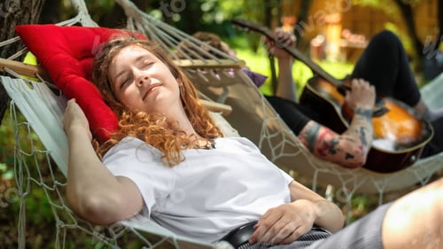 Preview: Couple lying on hammocks. Young man is playing guitar while woman is looking at him