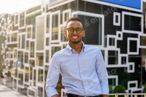 Preview: Portrait of handsome black African businessman smiling outdoors in city during summer