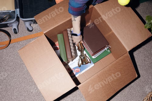 Preview: Teenager Packing Books and Trophy into Cardboard Box While Organizing Room