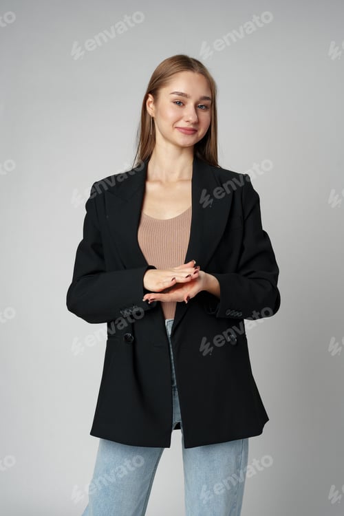 Preview: Young Woman in Casual Blazer and Jeans Smiling Against a Grey Background