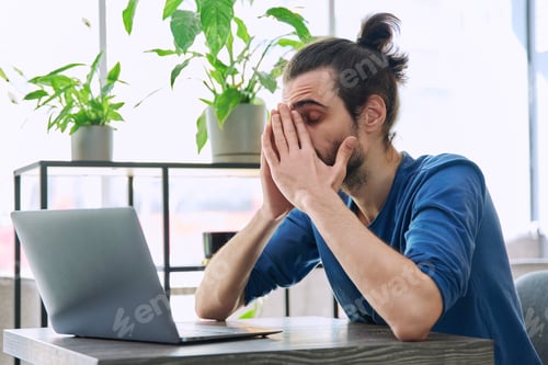 Preview: Young tired man working with laptop computer having headache fatigue
