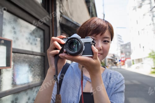 Preview: Woman standing outdoors, looking through a camera.