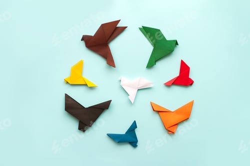 Preview: seven origami pigeons different colors in circle fly away from white bird on light blue background