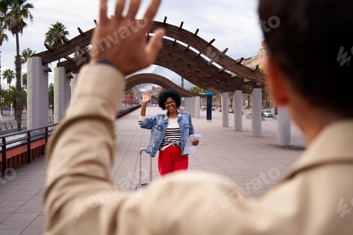 Preview: African American woman happily greeting her boyfriend with luggage outdoors after a long separation.