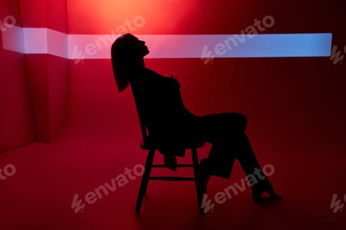 Preview: Woman on red background sits on chair, beam of light behind her face. Sexy