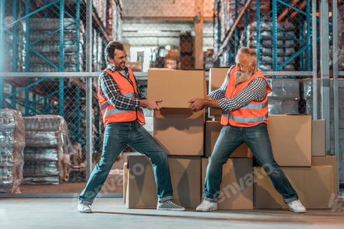 Preview: two male workers in vests holding box in warehouse