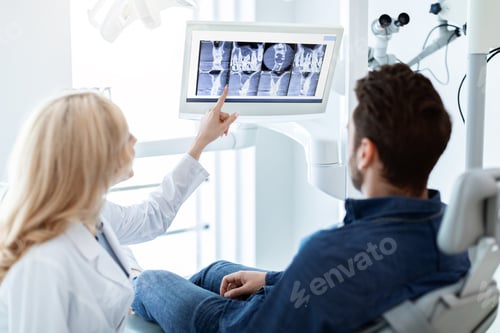 Preview: Woman dentist having conversation with patient, poitning at LED display
