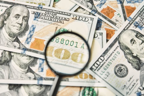 Preview: Magnifying glass on a pile of 100 dollar banknotes