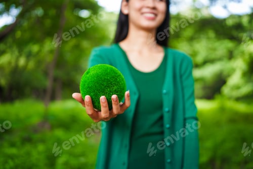Preview: An Asian woman holds a globe in green forest,symbolizing importance preserving nature.emphasizes