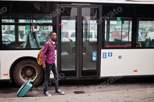 Young man waits by bus with rolling suitcase