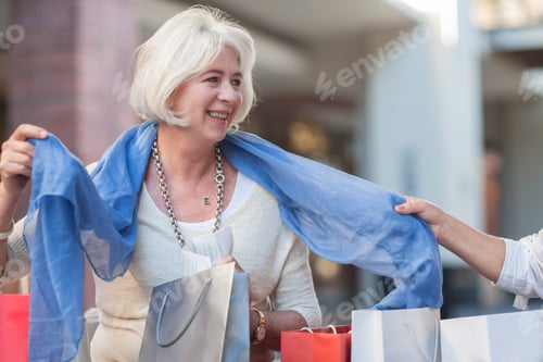 Preview: Mature woman trying on new scarf for friend in shopping mall
