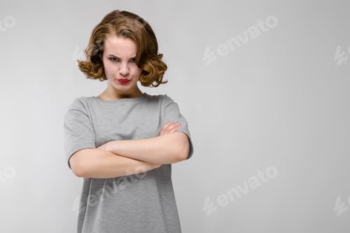 Preview: Charming young girl in a gray T-shirt on a gray background. The girl folded her arms over her chest