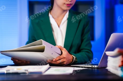 Preview: An Asian businesswoman works overtime,sitting her desk night,searching through numerous documents
