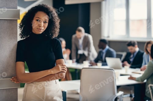 Preview: Confident African businesswoman keeping arms crossed while her colleagues working on background