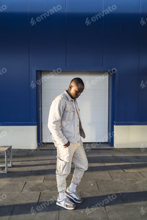 Preview: Vertical shot of a young Black male standing outdoors in front of a blue and white wall