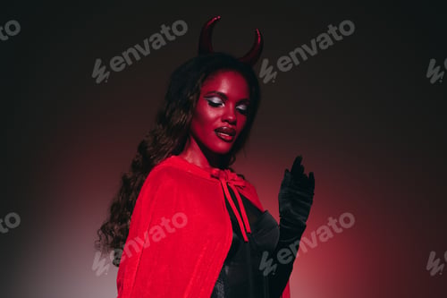 Preview: A stunning woman showcases a Halloween costume with a bold red cape and devil horns at night