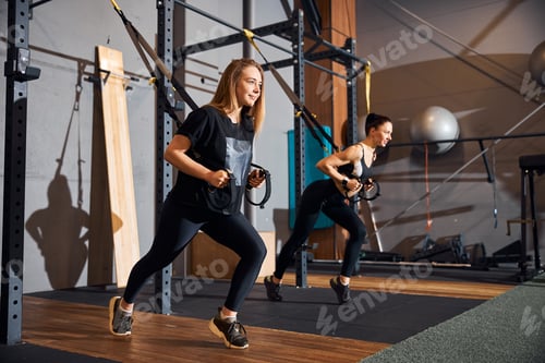 Preview: Joyous ladies doing physical exercises on gym equipment