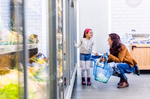 Preview: Happy mother and daughter at refrigerated section in supermarket