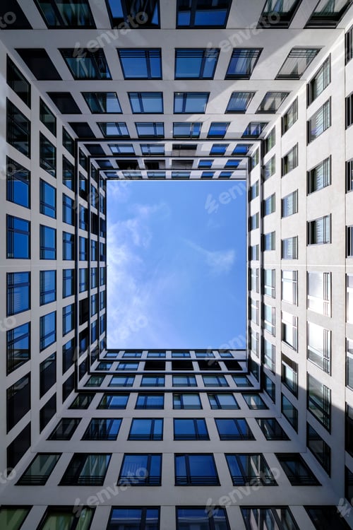Preview: Low angle shot of an urban high building with glass windows and walls under a blue sky