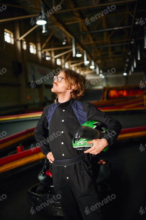 Preview: Man in Jumpsuit Holds Helmet on Racetrack
