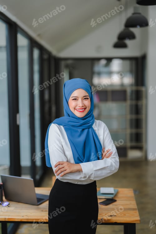 Preview: Smiling muslim businesswoman standing with arms crossed in modern office
