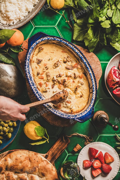 Preview: Female hands stirring Turkish lamb in sauce over green table