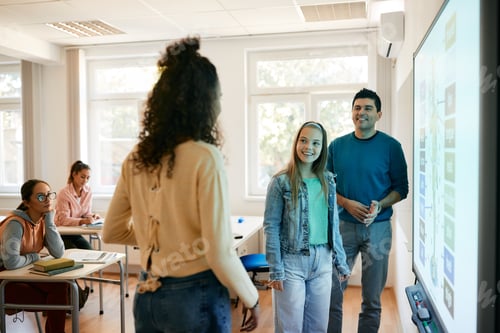 Preview: High school students and their teacher talking while using smartboard in the classroom.