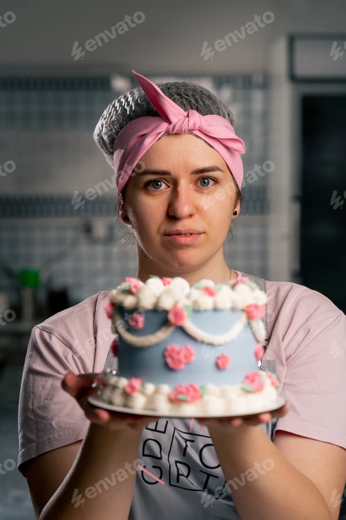 Preview: close-up in a professional kitchen a female baker stands with a finished cake in her hands