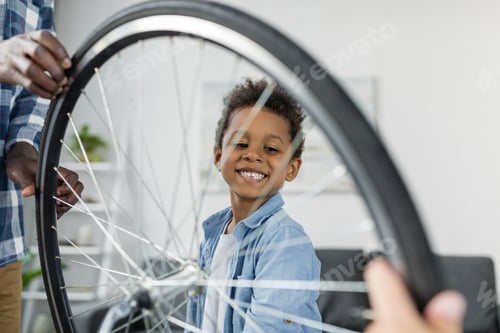 Preview: happy smiling african-american boy behind bicycle wheel