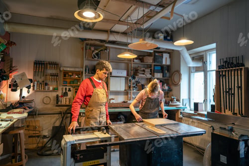 Preview: Carpenter man supervising novice woman working on circular saw table in woodworking workshop