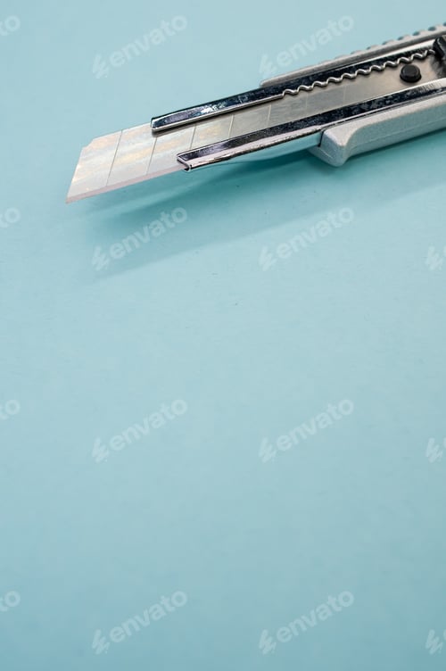 Preview: Vertical shot of a cutter blade tool isolated on blue background. Cutting knife for cardboard