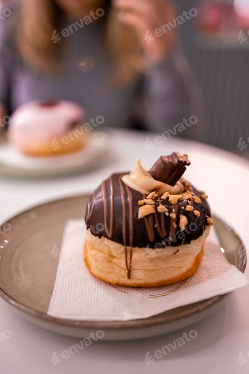 Preview: Delicious donut placed on a plate with a person enjoying dessert in a cozy cafe setting