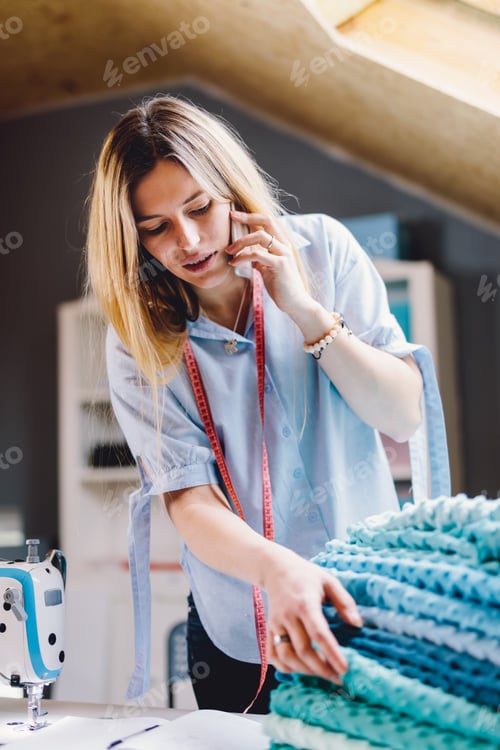 Preview: Seamstress smiling woman talking on mobile phone in sewing workshop