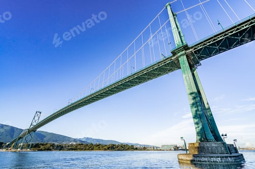 Preview: Low angle of a bridge going over a river under a clear blue sky