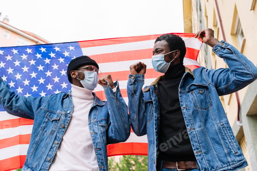 Preview: Low angle of cheerful African American male friends in masks standing with USA national flag on