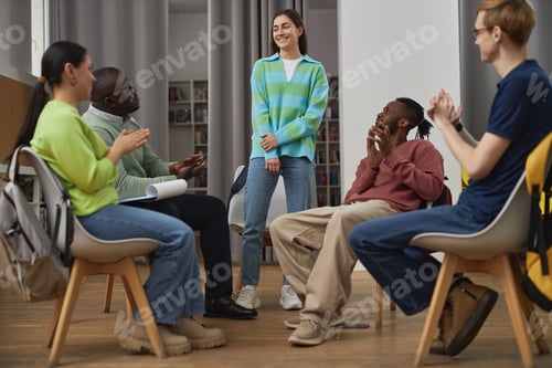 Vista previa: Diverse young people in support group circle with smiling young woman standing