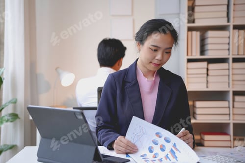 Preview: Young asian businesswoman analyzing financial data and reports while working