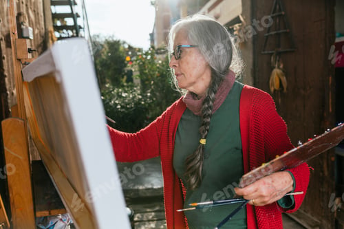Preview: Senior woman painting on canvas in garden