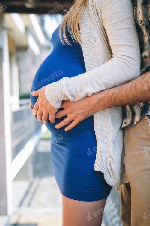 Preview: Close up of parents hands touching pregnant belly at home