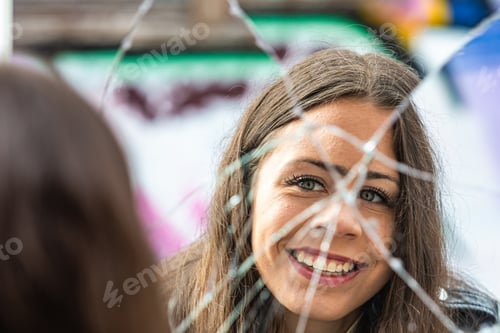 Preview: a young, beautiful woman looks at her reflection in a broken mirror