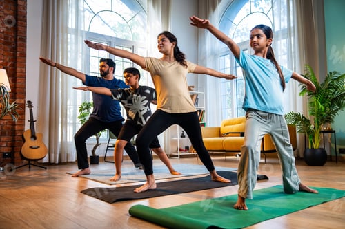 Preview: Indian parents and children performing warrior yoga pose indoors for strength and wellness