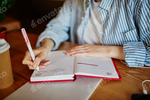 Preview: Faceless student writing in notepad in cafe